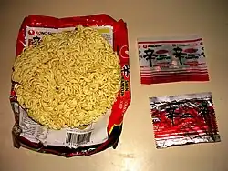 A package of Shin instant noodles, showing the noodle block, flavor packet, and dehydrated toppings.