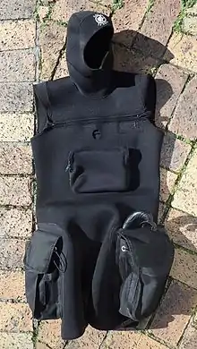 Sleeveless tunic in thin but abrasion resistant neoprene, with integral hood, two cargo pockets on the sides of the thighs, cross-chest zip closure, front pocket on the torso and opening for access to a dry-suit inflation valve. The tunic is suitable for wearing over most one-piece wetsuits for extra insulation, but mainly to support the cargo pockets and hood.