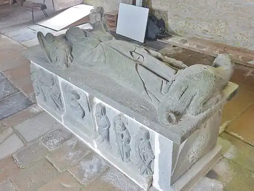 The gisant of Saint Nonne. The tomb is located in the middle of the nave and is 2.30 metres long. Note the dragon at her feet and the panels depicting the apostles around the base. Saint Nonne's feet point eastwards to the altar.