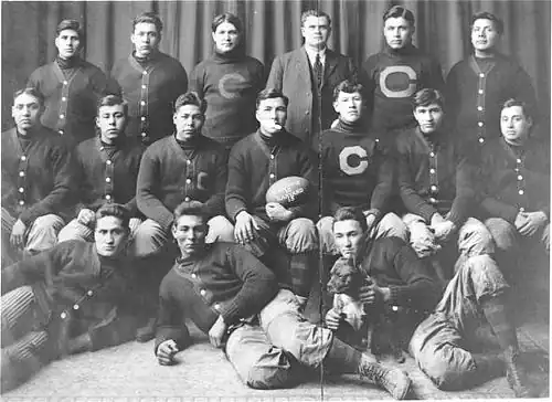 The 1911 Carlisle Indians football team pose with a game ball from the upset of Harvard. Coach "Pop" Warner (standing, third from right) and Jim Thorpe (seated, third from right) are pictured.