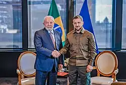 Lula and Zelenskyy shake hands while looking at the camera