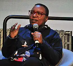 Meshell Ndegeocello speaking holding a mic in her left hand.