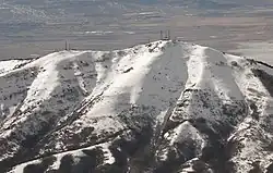 A snowcapped mountain with two clusters of communications towers at its peak