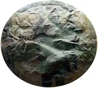 A bronze shield-facing, heavily dented, round in shape.