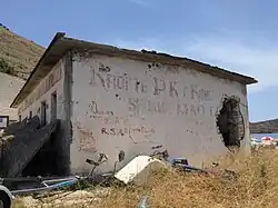 Abandoned building on Porto Palermo (side) with socialist message saying "Long live the Communist Party of China and comrade Mao Zedong" (RROFTE PK E KINES DHE SHOKUN MAO CE DUN)