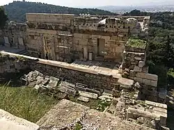 View downhill: the remains of the gate, partially ruined, can be seen below a low retaining wall.