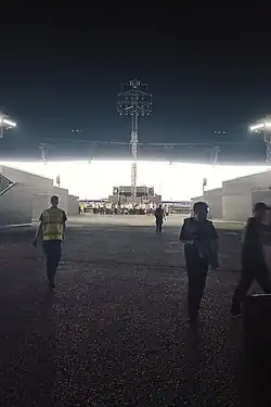 Men walk in front of a white screen in a stadium