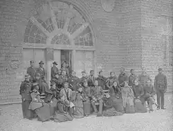 Black and white photograph of about twenty African Americans in formal attire, in front of a large brick building
