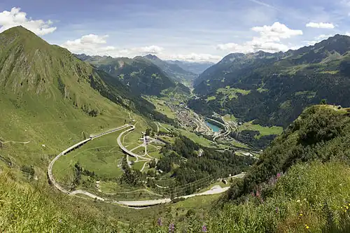 Photo of a looping road on the approach to Gotthard Pass with the town of Airolo in the distance.
