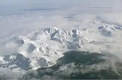 Aerial view of a range of icy mountains with a coastline visible in the foreground