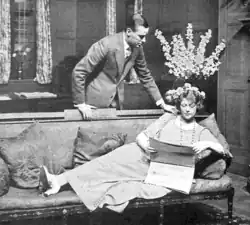 young man standing, young woman on a chaise-longue ignores him