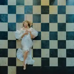 Aurora is wearing a white dress and lying on a checkered floor. She is looking sideways, while placing her hands in her chest.