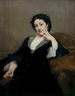 A seated woman gazes at the viewer, her right hand touching her chin in a thoughtful pose. She wears a dark dress with a white lace-trimmed collar and cuffs, seated in an ornate chair within a dark, muted background.