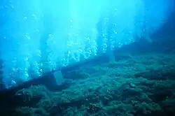 A pipe at the bottom of a body of water, with several holes which streams of bubbles are emerging from