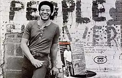 Withers smiling and leaning in front of a brick wall