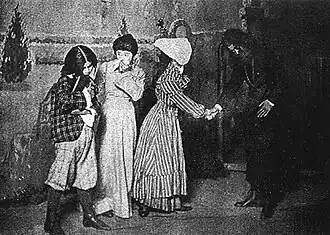 A black-and-white image of four people on a stage, a painted backdrop indicating an outdoor scene