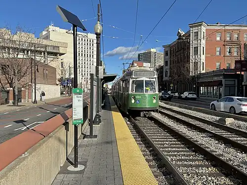 A light rail train next to a side platform in the median of an urban street