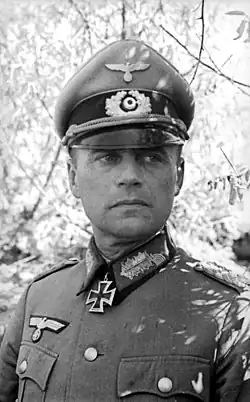 A man wearing a military uniform, peaked cap, and an Iron Cross displayed at the front of his uniform collar.