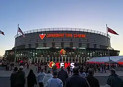 People milling about a large brick color building with large sign Canadian Tire Centre