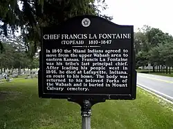 A historic marker with the following text, “CHIEF FRANCIS LA FONTAINE (TOPEAH) 1810-1847; In 1840 the Miami Indians agreed to move from the upper Wabash area to eastern Kansas. Francis La Fontaine was his tribe’s last principal chief. After leading his people west in 1846, he died at Lafayette, Indiana, en route to his home. The body was returned to his beloved Forks of the Wabash and is buried in Mount Calvary cemetery.”
