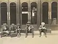Children reading books outside the main entrance of the Old Main, a library guard watched them from inside, black-and-white
