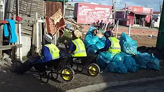 Street Cleaners in Joe Slovo Park, Dilapidated soccer field visible in the background