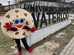 A cookie mascot stands in front of a sign that reads University of Waterloo and the Dana Porter Library