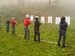 A line of people in front of targets drawing guns from holsters.