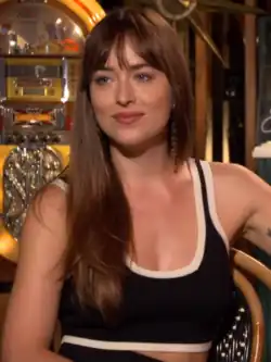 A dark-haired woman wearing a black shirt with white outlines sits on a chair