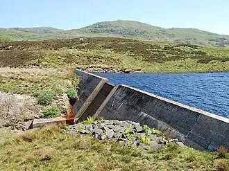 A concrete dam head, with spillway, surrounded by hills