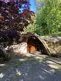 A gravel path leading to an arched entrance and wooden door partially obscured by a tree at the Mushroom House in Perinton, New York.