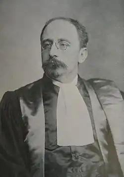 old black and white photo of a man in a black dinner jacket, with a moustache and glasses
