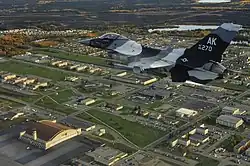 An F-16C Fighting Falcon from the 18th Aggressor Squadron flies over Eielson AFB in 2009. The base's largest hangar, known as the "Thunderdome," is visible in the bottom left of the image.