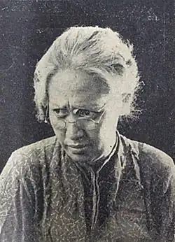 A profile portrait Fifi Young, made up as an old woman wearing glasses with white hair