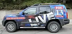 A KSTU news van, with Fox 13 logo and fox13now.com URL emblazoned on it, parked outside a building