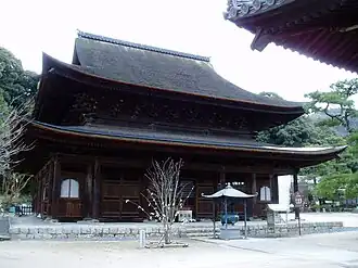 Large wooden building with a hip-and-gable roof and an enclosing pent roof.