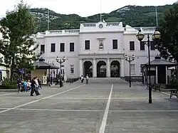 A long plaza with a large two—storey pink building at the far end, with a flight of steps leading up to the building's triple—arched entrance framed with columns.
