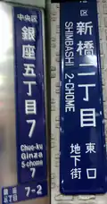 Two "chōmei-name plates" (町名板) including rōmaji for people unable to read the Japanese. (L) - A plate in standard style in larger cities. The letters on the plate indicates from the top Chuō Ward (中央区, Chuō-ku) and block 7, 5th chōme (銀座五丁目7, Ginza go-chōme nana). At the very bottom, 7-2 stands for block 7, number (banchi) 2. Pictured on the Ginza 4-chōme koban police box at the Ginza 4-chōme crossing, on Ginza main street facing to Wakō. (R) - Pictured is the one without any banchi numbers at the 2nd block in Shimbashi (新橋二丁目, Shimbashi ni-chōme). In Japanese writing at the bottom, it reads "you are in the underground city at the east gate" (東口地下街, Higashi-guchi chikagai), but the name for Shimbashi station is not indicated.