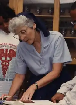 A nun in blue garb in a science lab points to a book with a student looking on