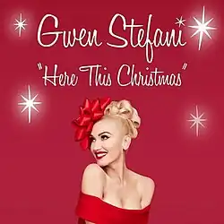 A red background displays a color photograph of American singer Gwen Stefani, dressed in a sleeveless red gown and adorned with a red ribbon on her head, worn as a headband; the image also contains 4 large white sparkles and the words: Gwen Stefani, "Here This Christmas"
