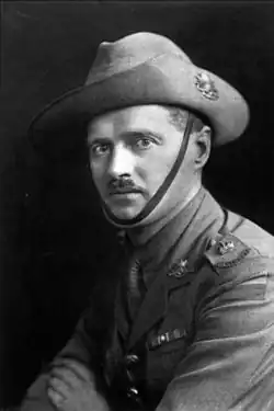 A head and shoulders portrait of a moustachioed man in military uniform. He is wearing a slouch hat, and has his arms crossed half-facing the camera.