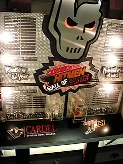 A large silver, metal display hanging high on a wall. It features winners of four awards and miniature replicas of two trophies.