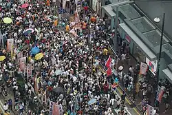 Hundreds of people marching down a road in Hong Kong next to roadside banners of different political parties on 1 July 2016.