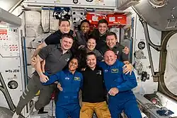 The seven Expedition 71 crew members gather with the two CFT crew members for a portrait aboard the ISS