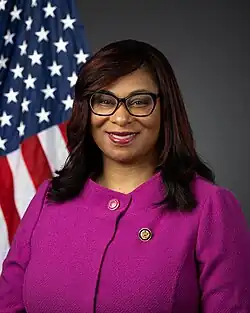Bynum smiling in front of the U.S. flag, wearing her House member pin and a pink jacket.