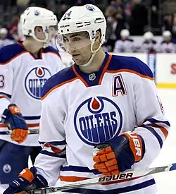 Ice hockey player in an orange, white, and blue Edmonton Oilers jersey with a letter A on the top right