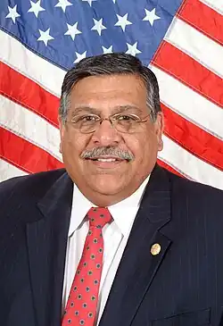 Juan Manuel Escobar in a suit with a red tie in front of the flag of the United States.