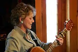 Lacy J. Dalton, playing an acoustic guitar.