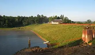 A body of water surrounded by green grass with in a house to the right side and trees in the distance.