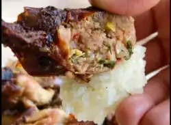 A person is holding a slice of sausauge on top of sticky rice